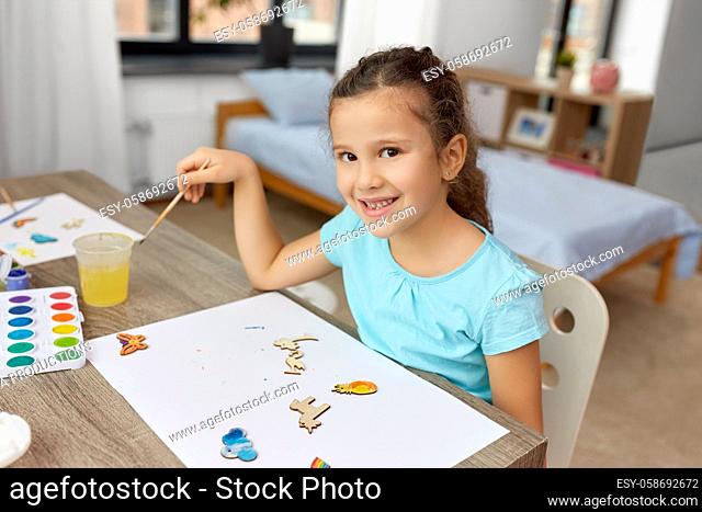 little girl painting wooden items at home