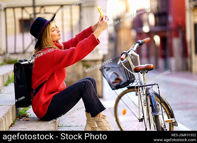 Woman taking selfie through mobile phone while sitting by bicycle on steps