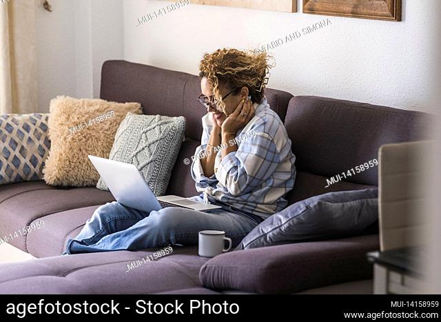 beautiful young woman in eyeglasses working on laptop while drinking coffee sitting on sofa. surprised businesswoman in casuals working from home