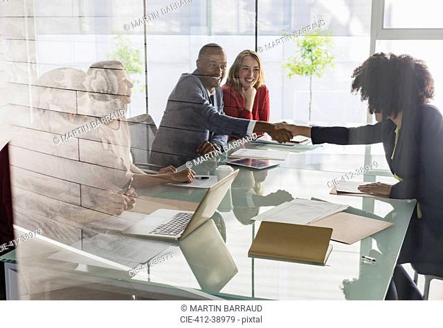 Businessman and businesswoman handshaking across conference table in meeting