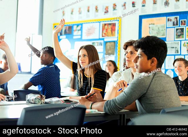 High school students with hands raised, asking questions during lesson in classroom