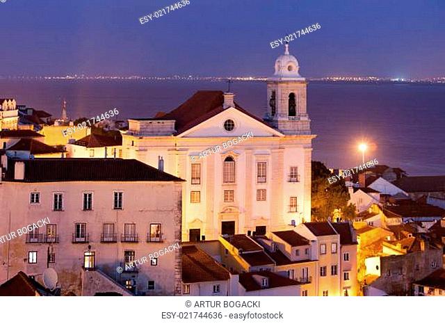 Santo Estevao Church at night in old Alfama district of Lisbon in Portugal, Tagus river in the background