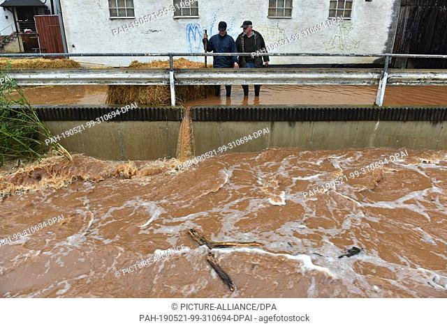 21 May 2019, Hessen, Lohfelden: Two men look out from their farm at the floods of the Losse. Heavy rainfall has caused numerous streams in northern Hesse to...