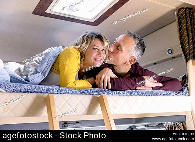 Man kissing woman lying on bed in camper van
