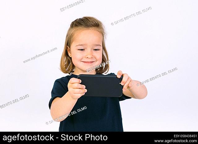 Little blonde girl with mobile phone in her hands, playing a game