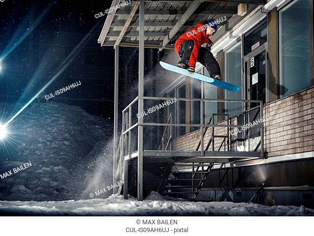 Mid adult male snowboarder jumping mid air from building at night
