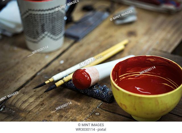 Close up materials in a Japanese porcelain workshop, bowl with red paint, pestle and paintbrushes