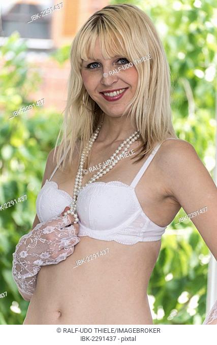 Young woman wearing white lingerie with a pearl necklace around her neck, outdoors