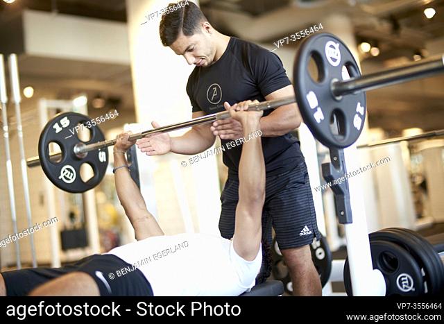 Personal trainer assisting man lifting weights in gym
