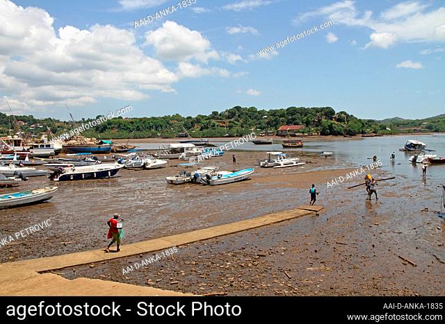 Beached boats and man carrying log in Andoany Harbour or Hell-Ville Harbour, Nosy Be, Madagascar