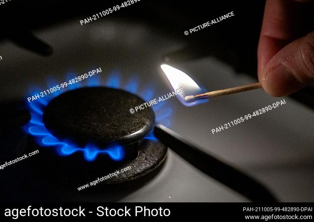 05 October 2021, Baden-Wuerttemberg, Stuttgart: A gas flame is lit on a kitchen stove with a match. Gas and electricity are more expensive in Europe than they...