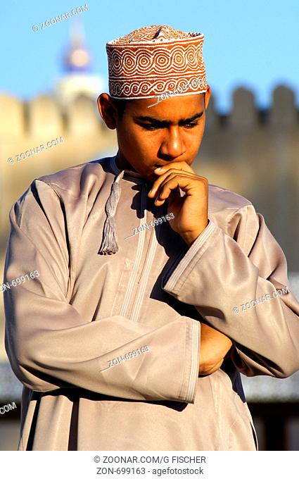 In Gedanken versunken, Omani Junge in der Nationaltracht Dishdasha und einer Kummah Kappe als Kopfbedeckung, Nizwa, Sultanat Oman / Absorbed in thoughts