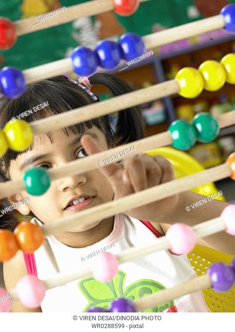 South Asian Indian girl sitting in front of abacus and calculating beads sliding on wires in nursery school MR