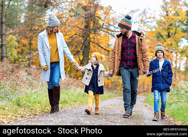 Family holding hands while walking on footpath at forest during autumn