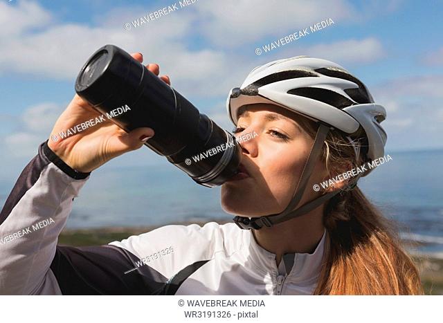 Female biker drinking water from bottle on a sunny