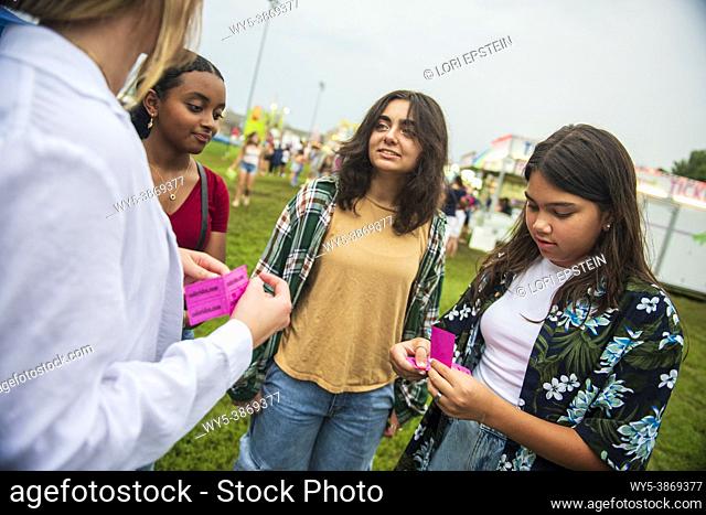 A happy, diverse group of girl friends share tickets at the county fair on a summer night