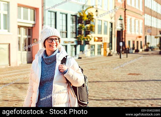 Portrait of a young Caucasian European woman tourist in glasses for the view of a white hat and a down jacket with a black backpack posing on an old Europe...