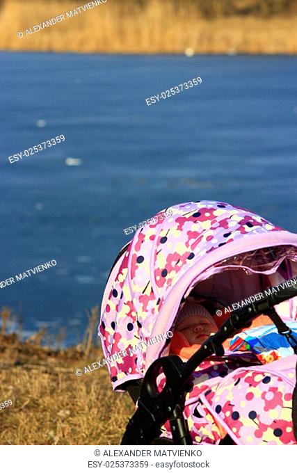little baby sleeps in the perambulator at the fresh air near the river