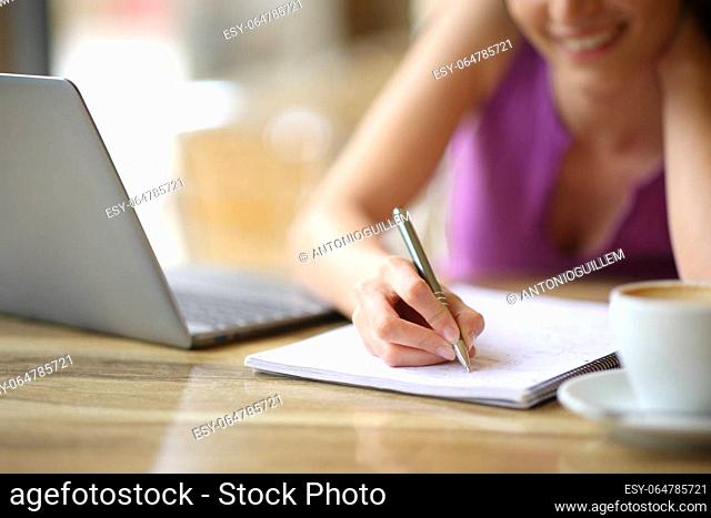 Close up of a happy student hand taking notes in a coffee shop terrace