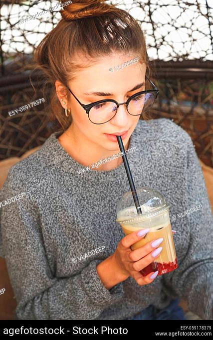 Close up portrait of young millenial hipster woman drinks cocktail in outdoors cafe. Casual dressed in eyeglasses