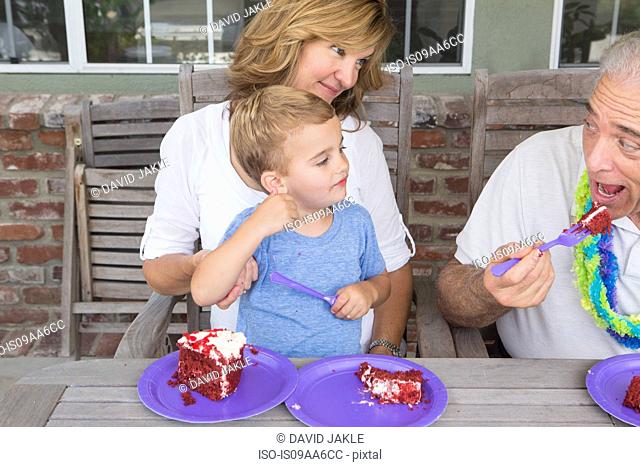 Grandson and mother watching senior man eat birthday cake