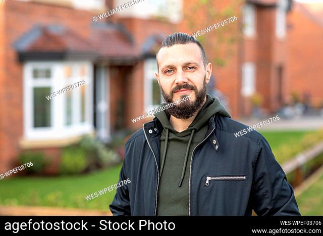 Confident bearded man standing outside new home