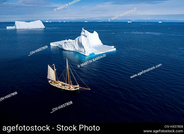 Ship sailing past majestic icebergs on sunny blue Atlantic Ocean Greenland