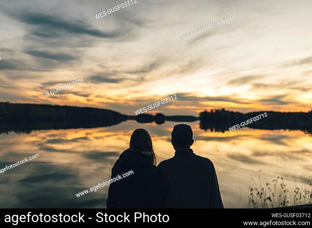 Couple sitting at lake, watching sunset