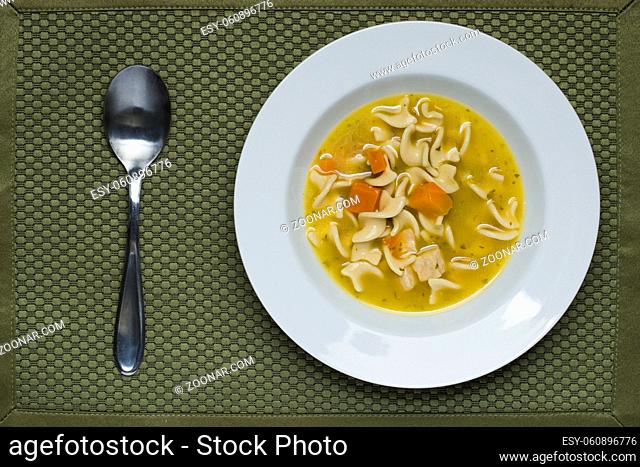 An overhead view of a bowl of chicken noodle soup and a spoon on the side