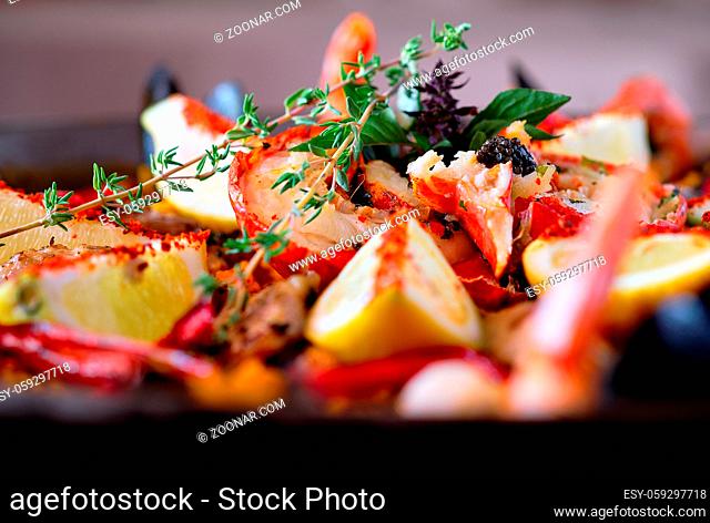 Close up image ripe ingredients of prepared served paella spanish traditional cuisine, bright colors. Dish garnished with lemon slices