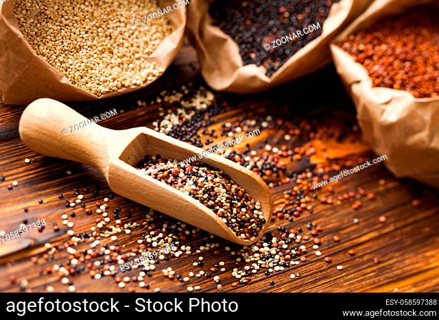 Mix of quinoa seeds in the wooden scoop. White, red and black quinoa in paper bags on the background