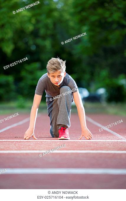 deep front full body view of a young male teenager looking in depth starting position on a tartan track in the camera