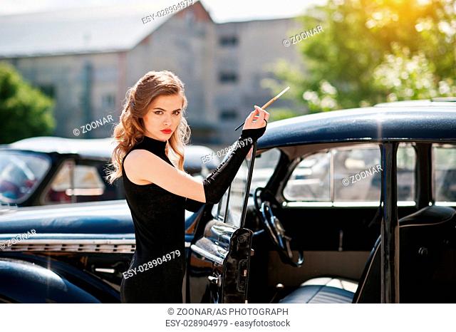 Portrait of beautiful sexy fashion girl model with bright makeup in retro style near vintage car with a cigarette in hand