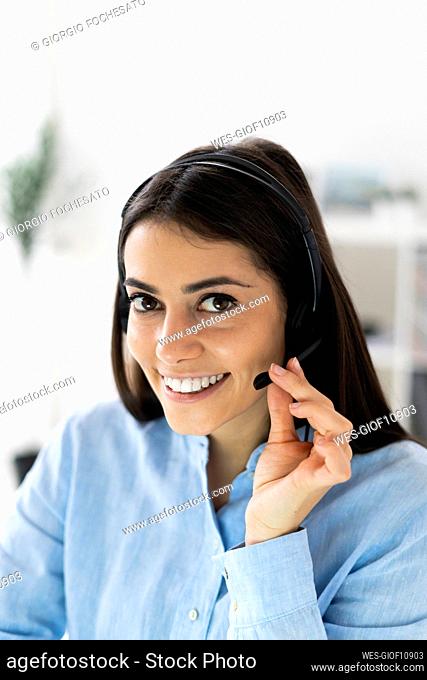 Smiling businesswoman adjusting microphone headset while sitting at office