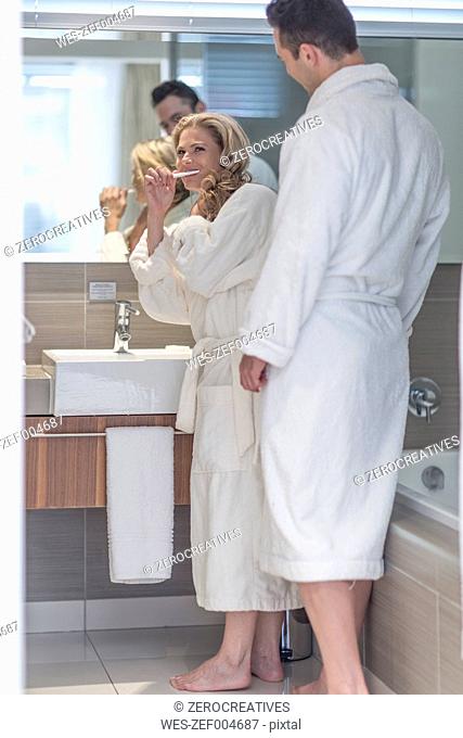 Couple wearing white bathrobes together in a hotel bathroom