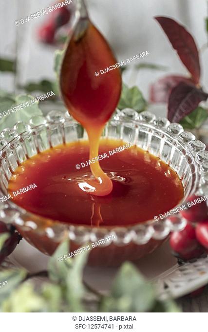 Rose hip jam dripping from a spoon into a glass bowl