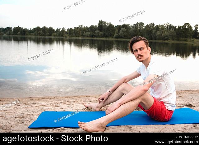 Young man relax siting on beach looks to right with sky. Conceptual for thinking and looking for concentrate somethings in Summer background