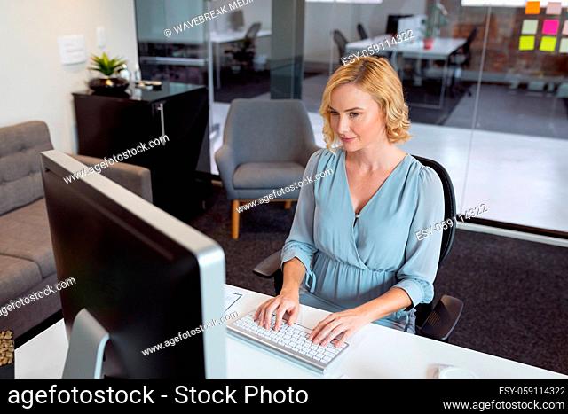 Smiling caucasian businesswoman sitting at desk in office using computer