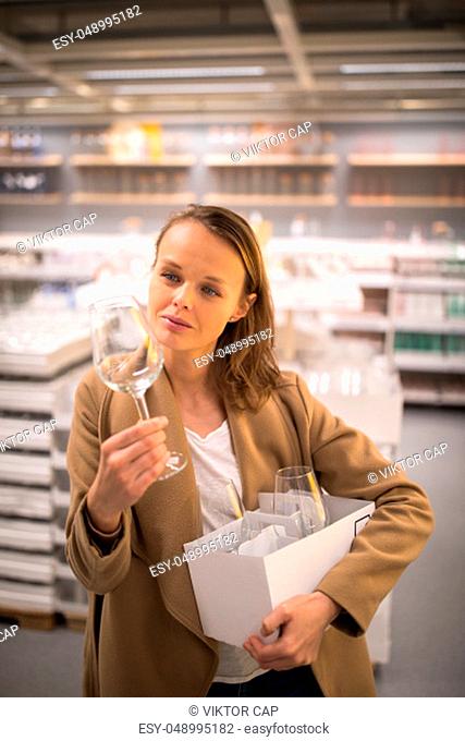 Pretty, young woman in a home supply store choosing the right glasses for her wine addiction (color toned image; shallow DOF)