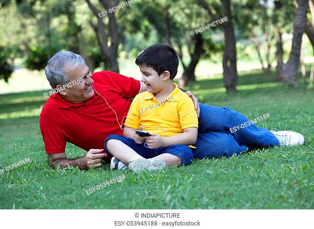 Grandfather and grandson listening to music in a park