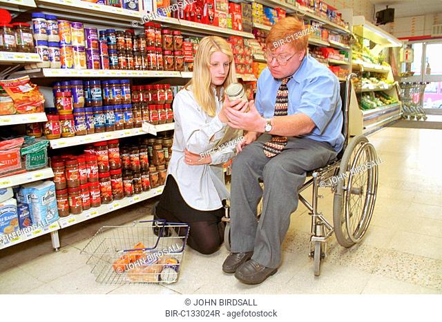 Man, who is wheelchair user, shopping in supermarket with assistance of teenage carer