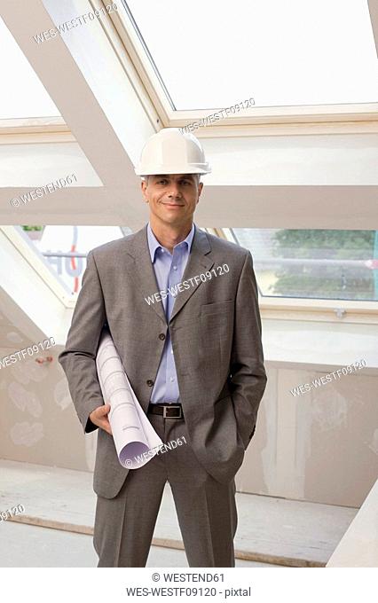 Architect at construction site holding construction plan, smiling, portrait