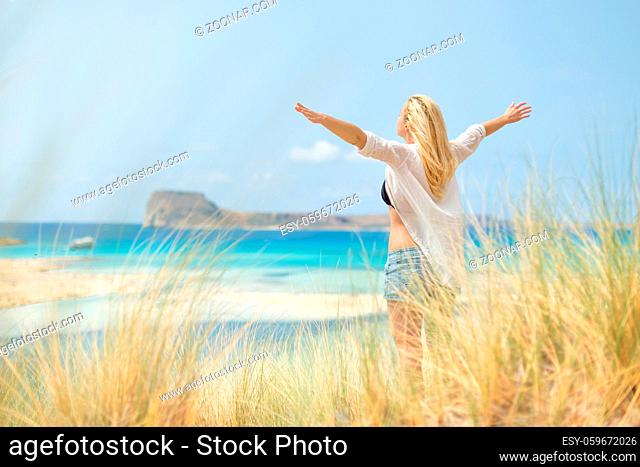 Relaxed woman, arms rised, enjoying sun, freedom and life an a beautiful beach. Young lady feeling free, relaxed and happy