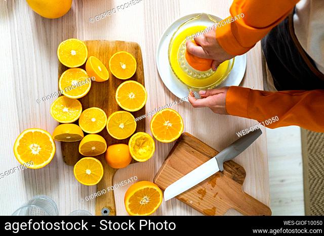 Woman preparing orange juice on juicer while standing by table at home