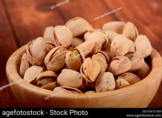 Pistachios in a wooden bowl on wooden surface, pile of pistachios, roasted pistachios in a bowl