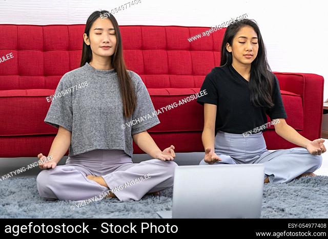 Two asian Woman do meditate from online meditation coaching to relax and reduce stress and strain for good mental health cause from city lockdown from...