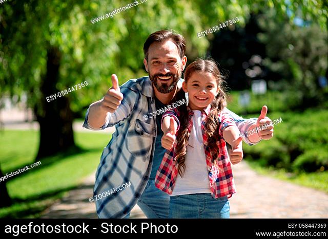 Happy Father And Daughter In City Park Showinh Together Thumb up. City Park On The Background. Happy Loving Family Concept