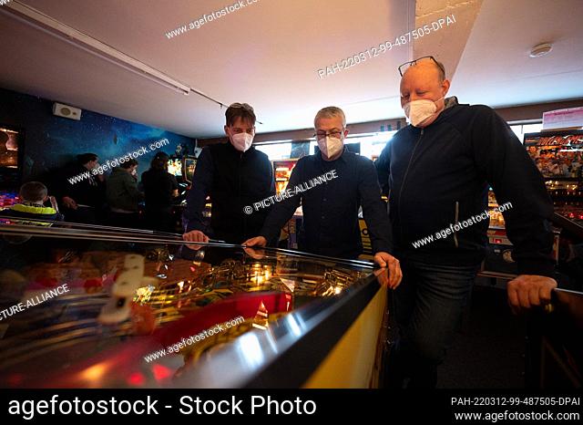 PRODUCTION - 05 March 2022, Hessen, Seligenstadt: Three men play pinball at the Pinball and Arcade Museum. The museum, which is run by the association For...