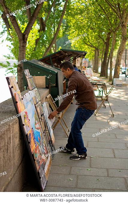 Traditional books and gifts seller (bouquiniste) organizing the display of his products next to the banks of the Seine. Paris, France