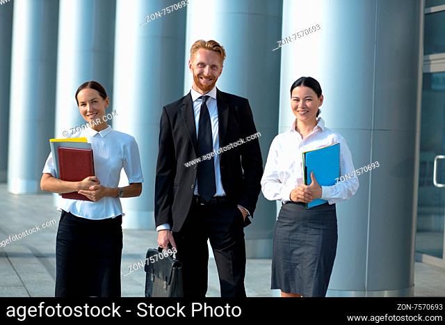 Happy business people in group walking near office building. Women with folders and man with brief case happy smiling for the camera